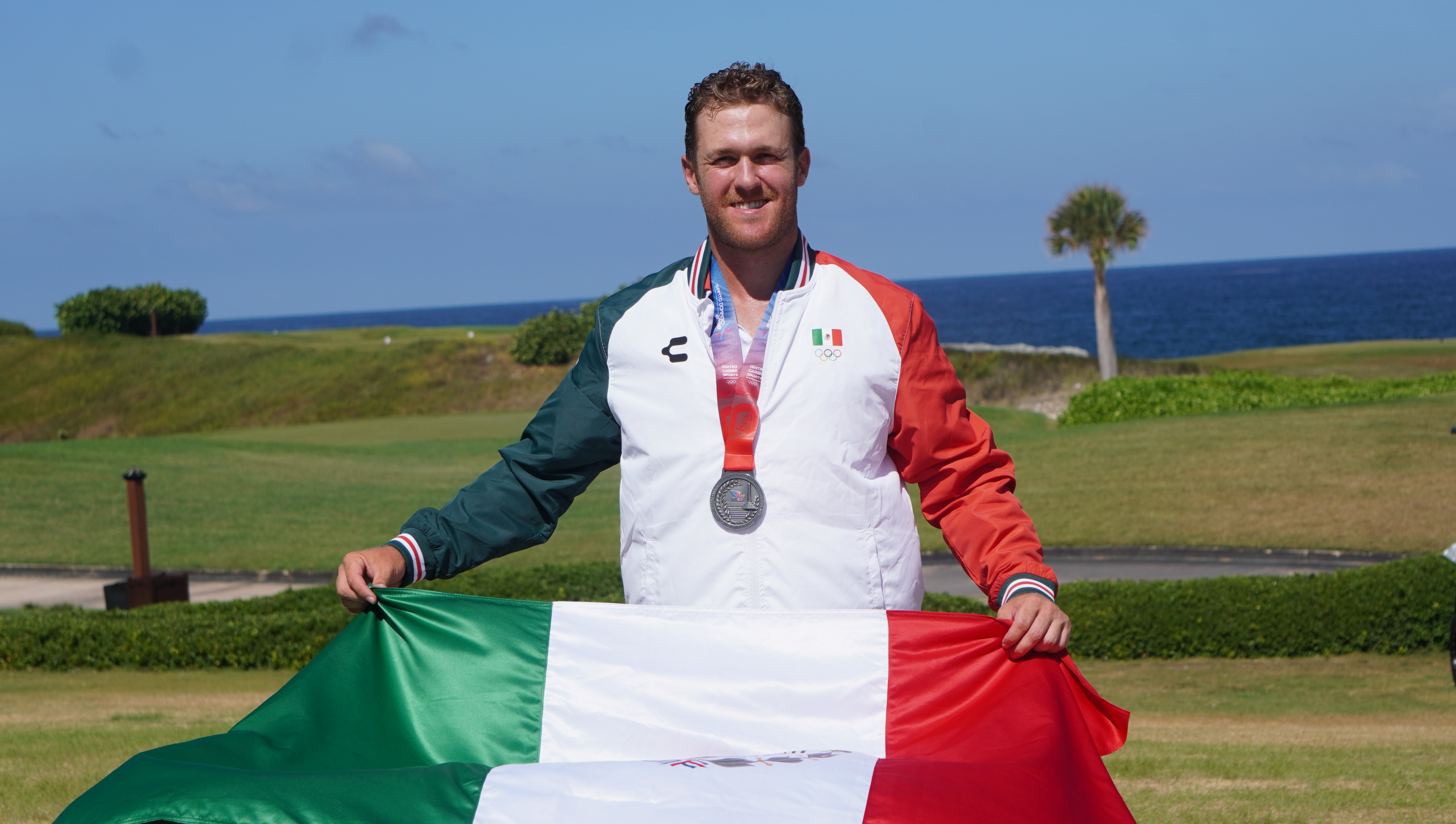 Luis Carrera con la medalla de plata y la bandera de México en un campo de golf